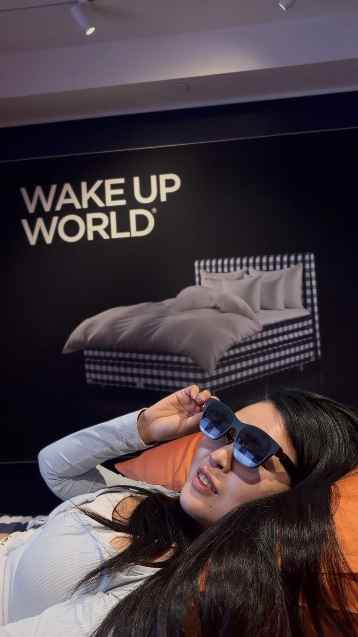 Tester reclining with Dreama glasses near Wake Up World signage.
